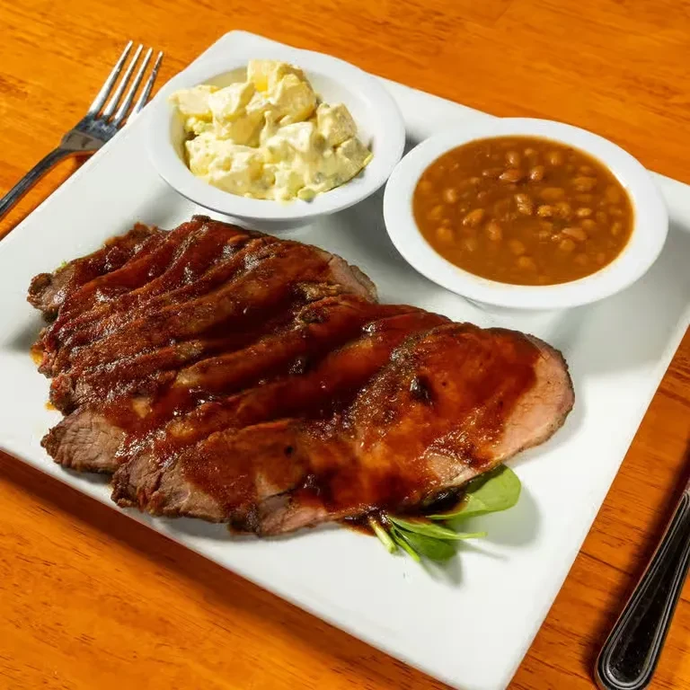 Sliced roast meat with sauce, potato salad, and baked beans.