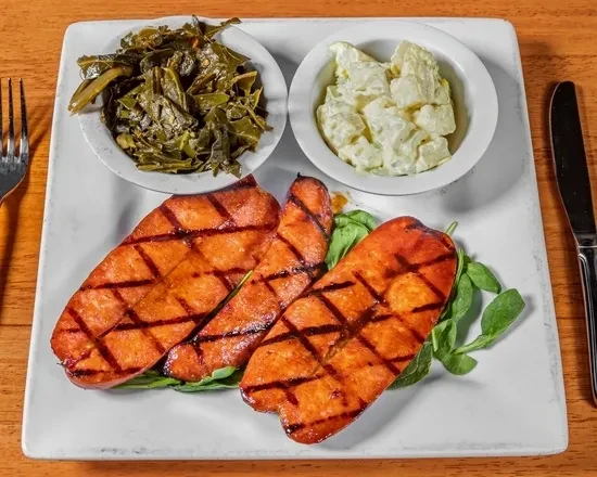 Grilled ham, collard greens, potato salad, fork and knife on a plate.