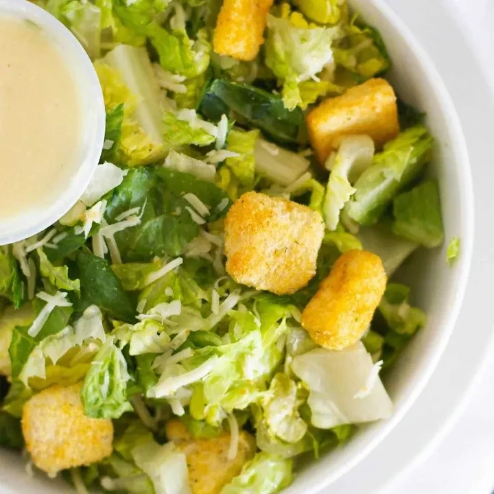Salad with Romaine, Parmesan, croutons, and dressing in a white bowl.