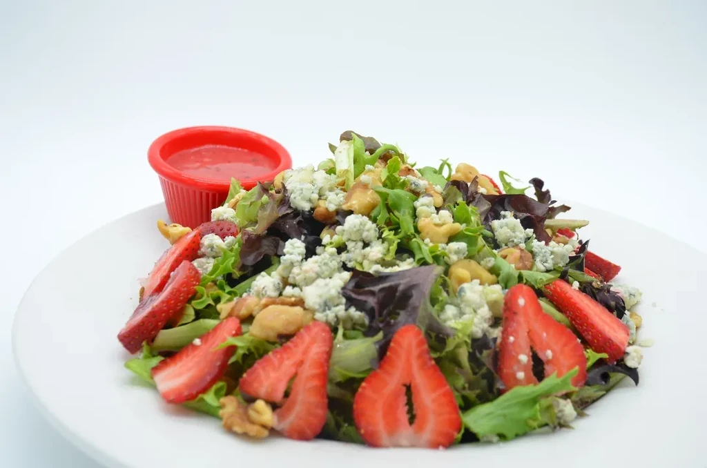 Mixed greens salad topped with blue cheese, walnuts, strawberries, and dressing.