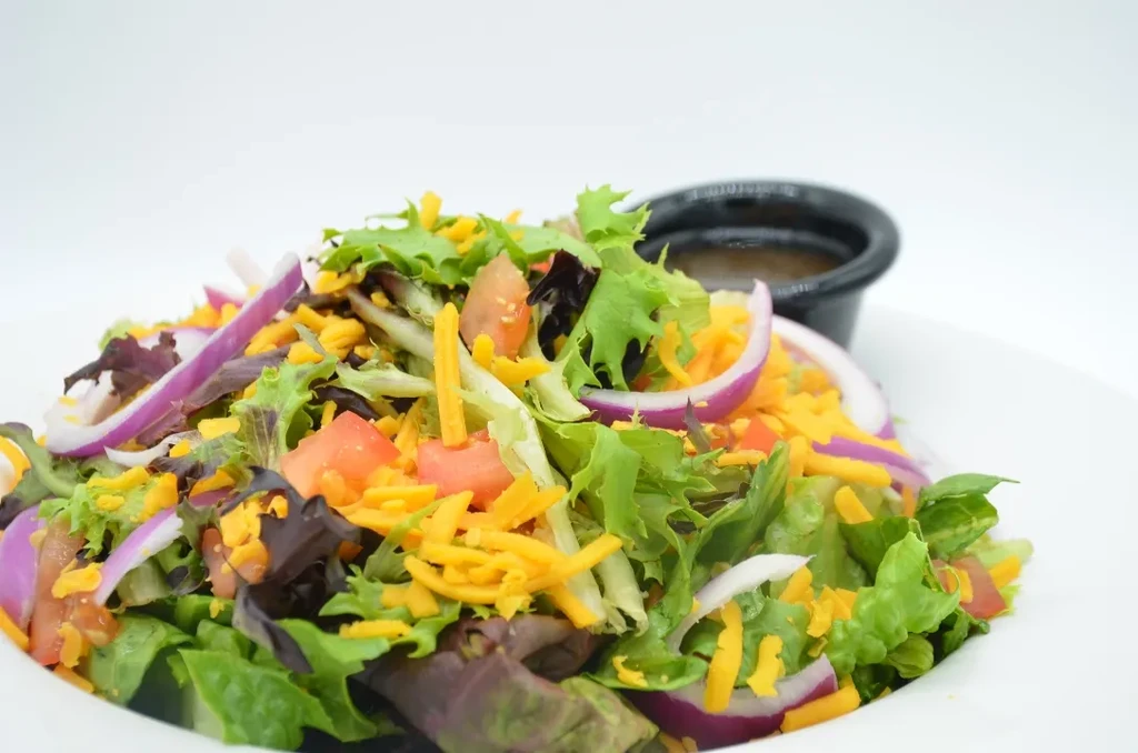 Fresh green salad with tomatoes, red onion, shredded cheese, and dressing.