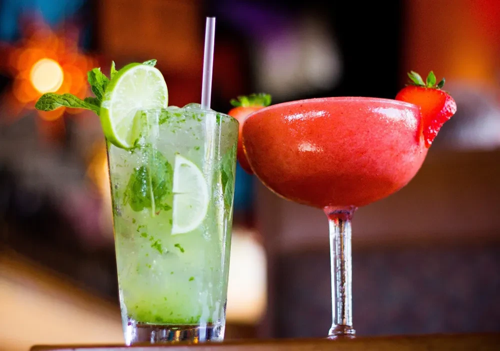 Two garnished cocktails, one green and iced, one red and frozen.