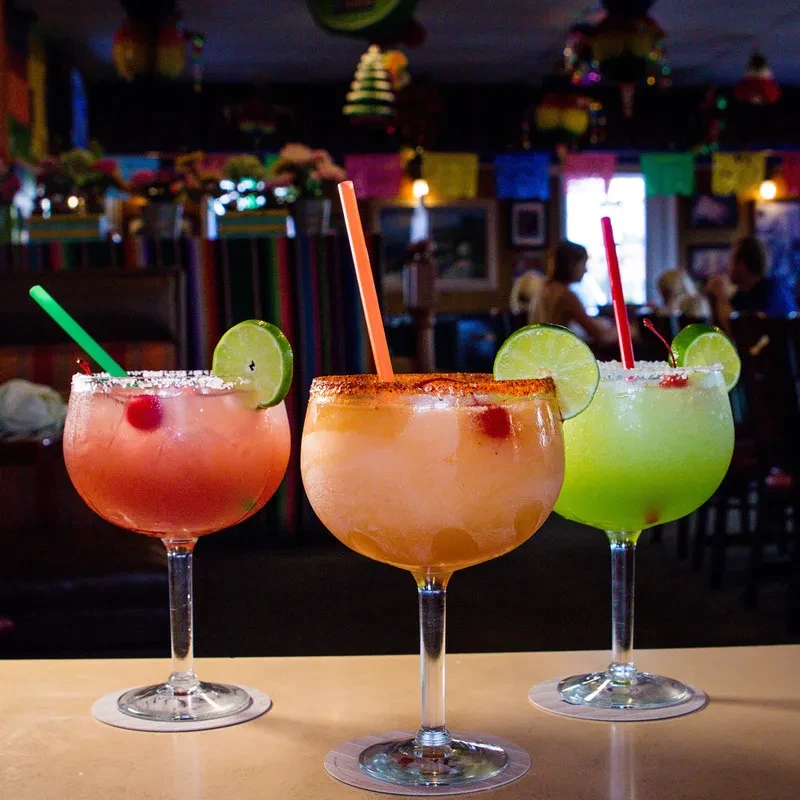 Three colorful, garnished margaritas with various rims in a lively bar.