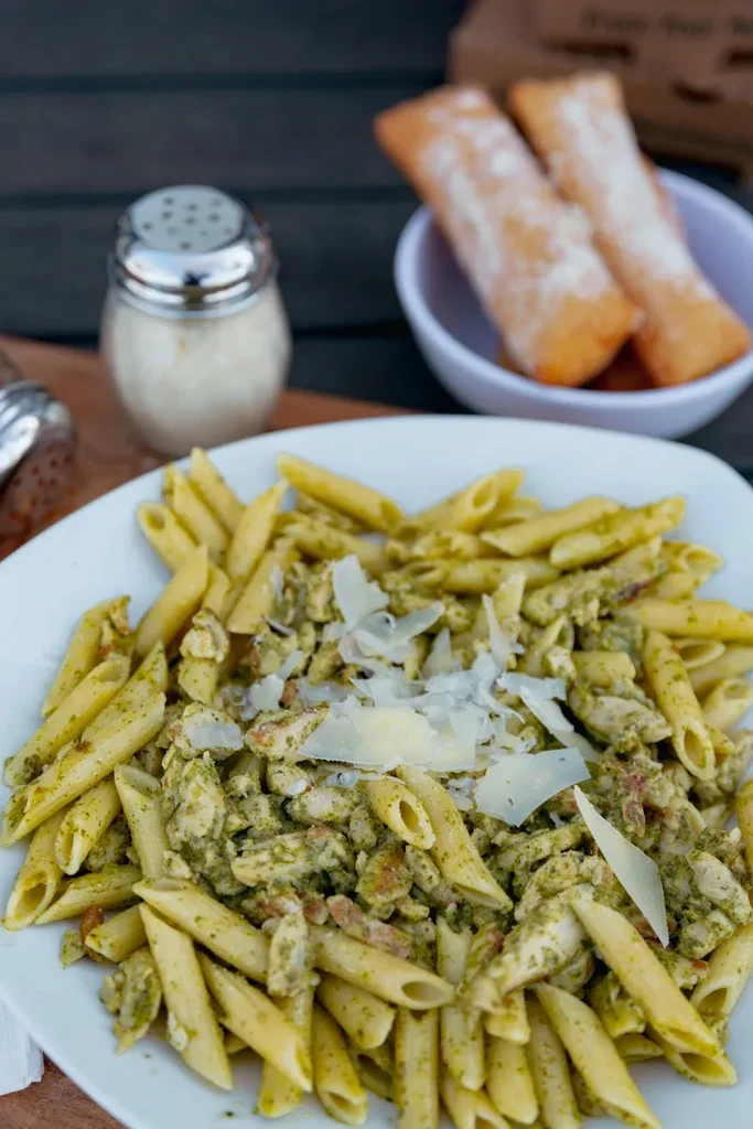 Plate of penne pasta with pesto, chicken, and Parmesan cheese.