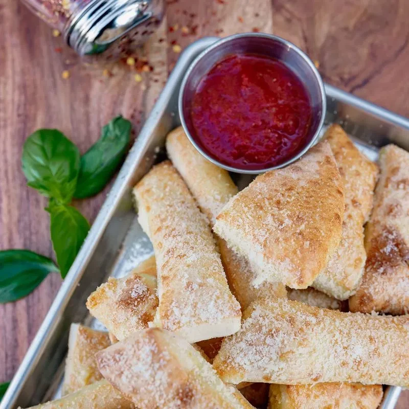 Parmesan breadsticks, marinara sauce, red pepper flakes, and basil in silver tray.
