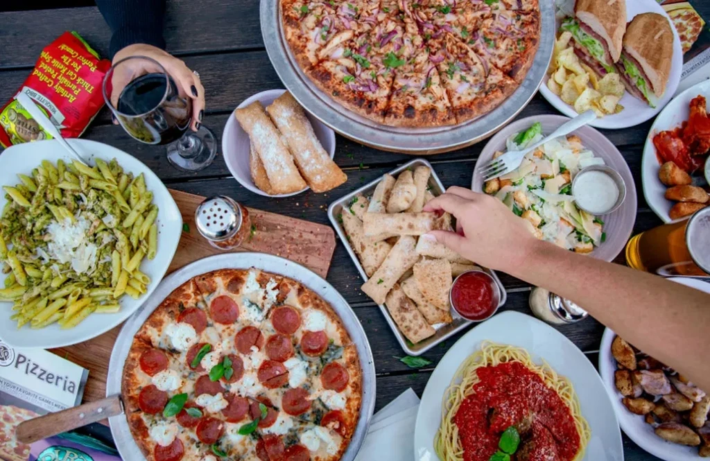 Overhead view of a lavish Italian-American food spread with hands reaching.
