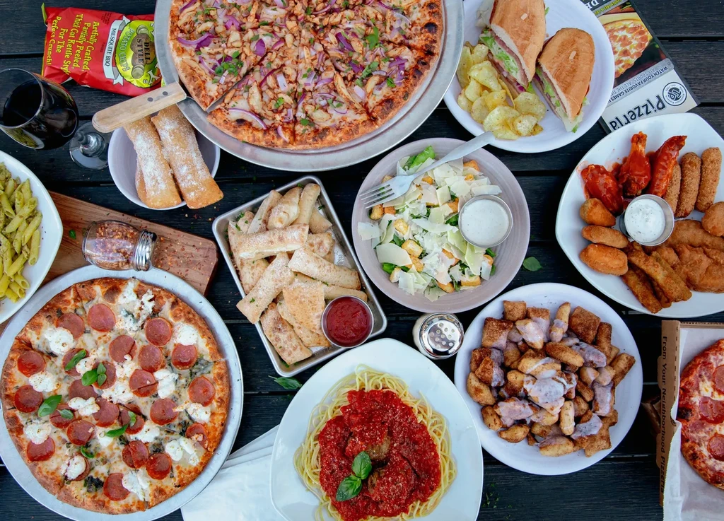 Large spread of Italian-American pizzas, pastas, sandwiches, and fried appetizers.