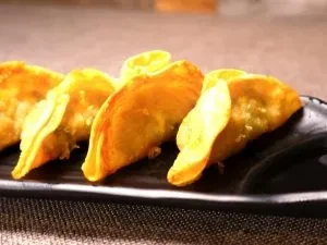 Plate of five golden-brown fried dumplings with crimped edges.