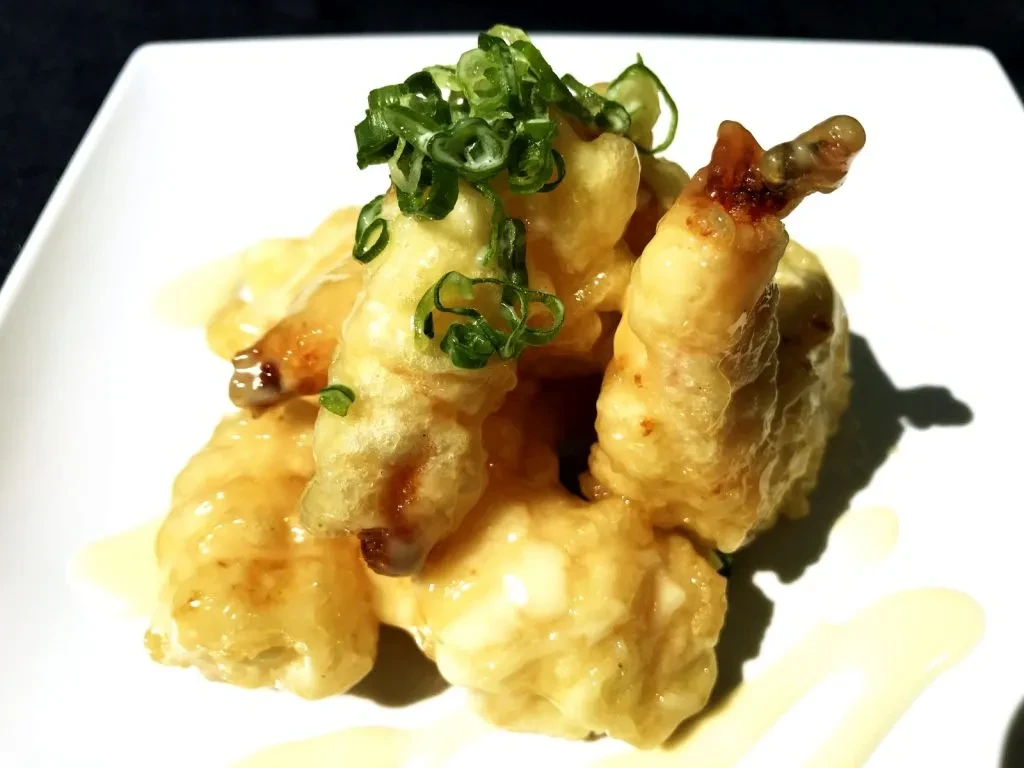 Deep-fried shrimp, creamy sauce, and green onions on a white plate.