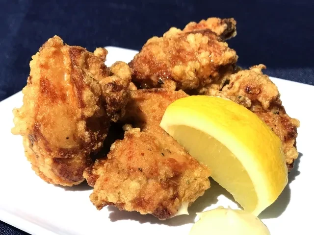 Golden fried chicken karaage, lemon, and sauce on a white plate.