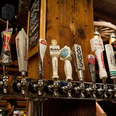 Close-up of nine diverse beer tap handles on a rustic bar.