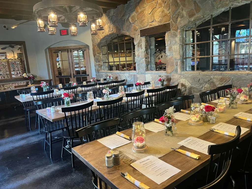 Rustic dining room with decorated wooden tables, stone wall, and chandelier.