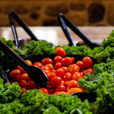 Piled red cherry tomatoes, green leafy vegetables, and serving tongs.
