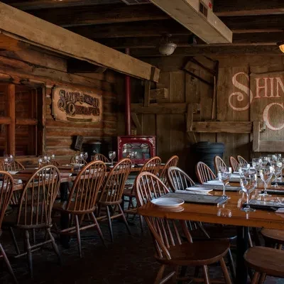 Rustic restaurant interior with wooden tables, chairs, log walls, and stove.