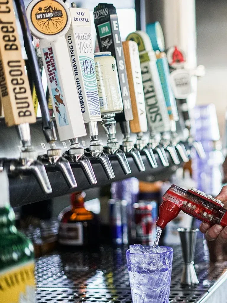 Hand pouring drink below various craft beer taps at a bar.