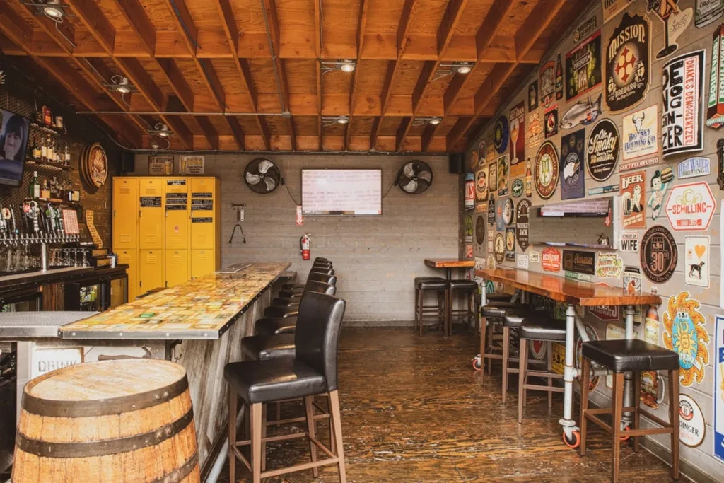Empty industrial-rustic bar with exposed beams, stocked bar, and eclectic signage.