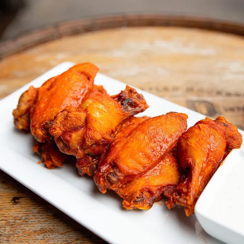 Close-up of crispy orange-red chicken wings with dipping sauce on wood.