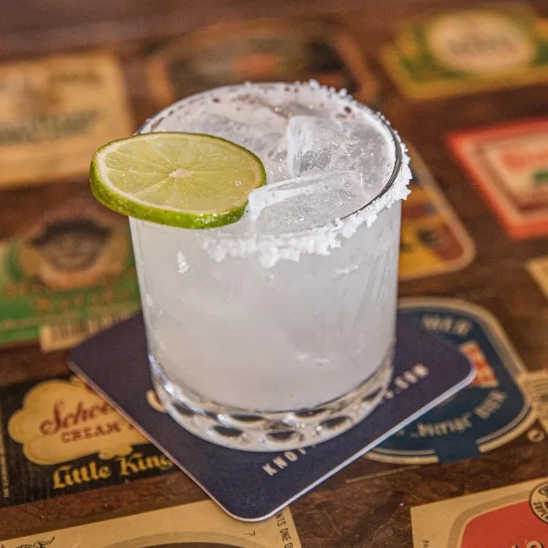 Margarita with salted rim, lime, and ice on a wooden bar surface.