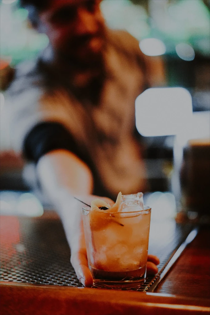 Hand holds an amber cocktail with ice, orange peel, and dark berry.