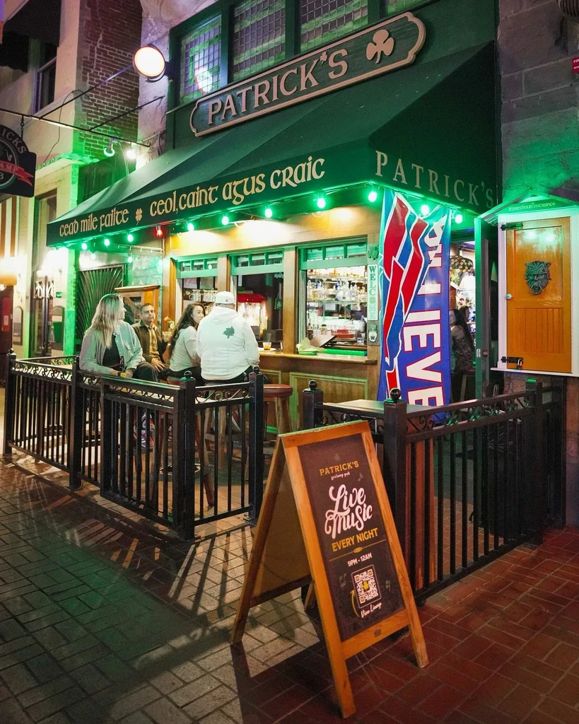 Green-lit exterior of Patrick's Irish pub at night with patrons.