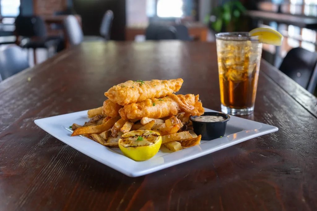 Plate of golden fish and chips, sauce, grilled lemon, and drink.