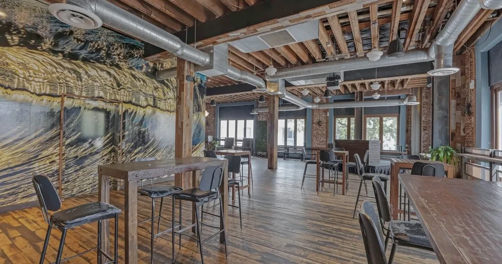 Modern rustic-industrial restaurant with exposed beams, abstract mural, and high-top tables.