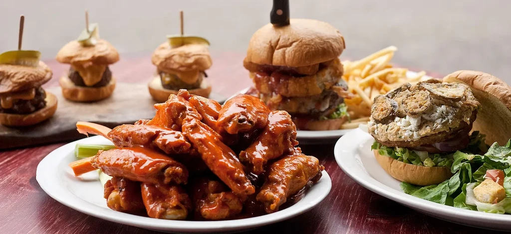 Buffalo wings, multiple burgers, fries, and salad spread on a wooden table.