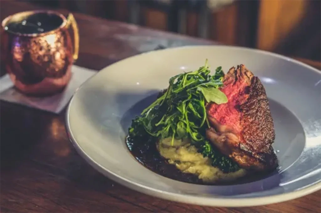 Seared steak with arugula, mashed potatoes, and sauce; copper mug.