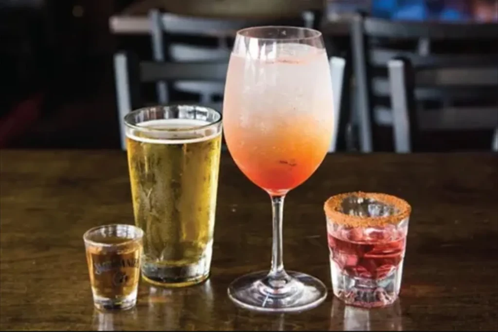 Four alcoholic drinks: beer, layered cocktail, and two shots on a wooden table.