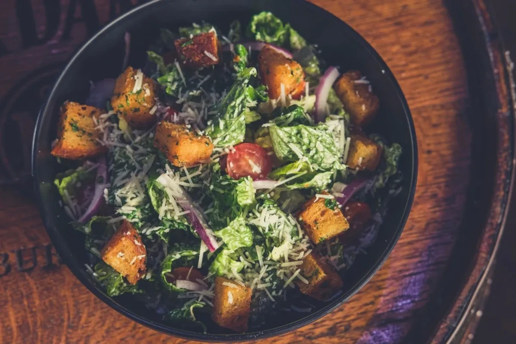 Caesar salad with lettuce, cheese, croutons, tomatoes, red onion on wood.