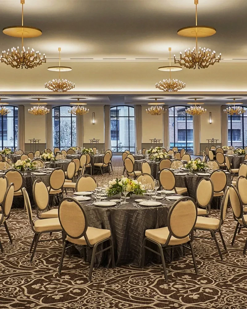 Dining hall set with round tables, white flowers, and gold chandeliers.