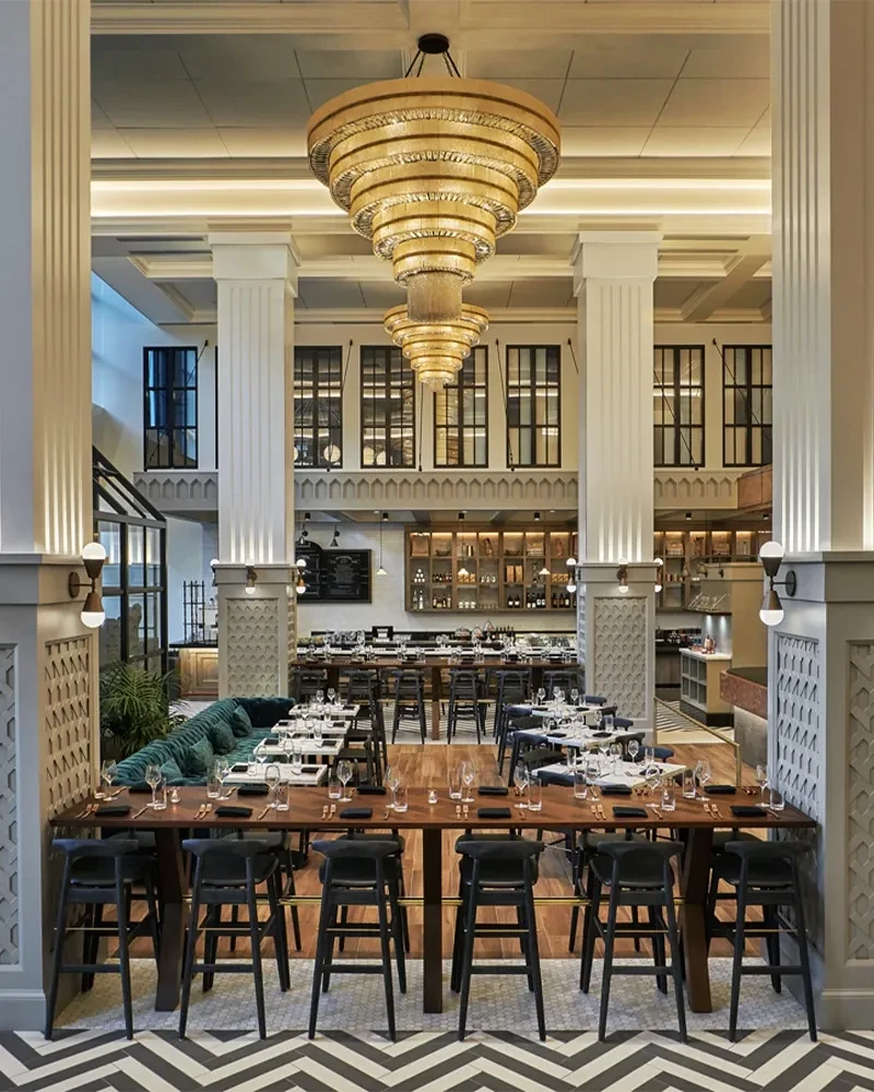 Elegant, empty restaurant interior with columns, communal table, and chandelier.