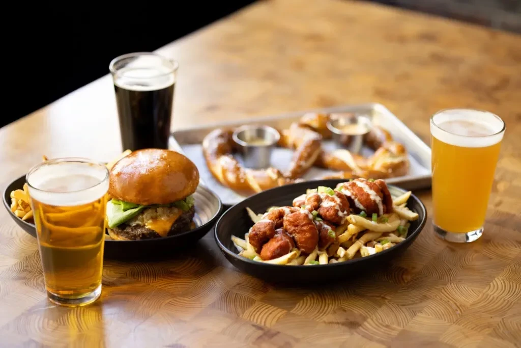 Rustic table spread with cheeseburger, chicken fries, pretzels, and beers.