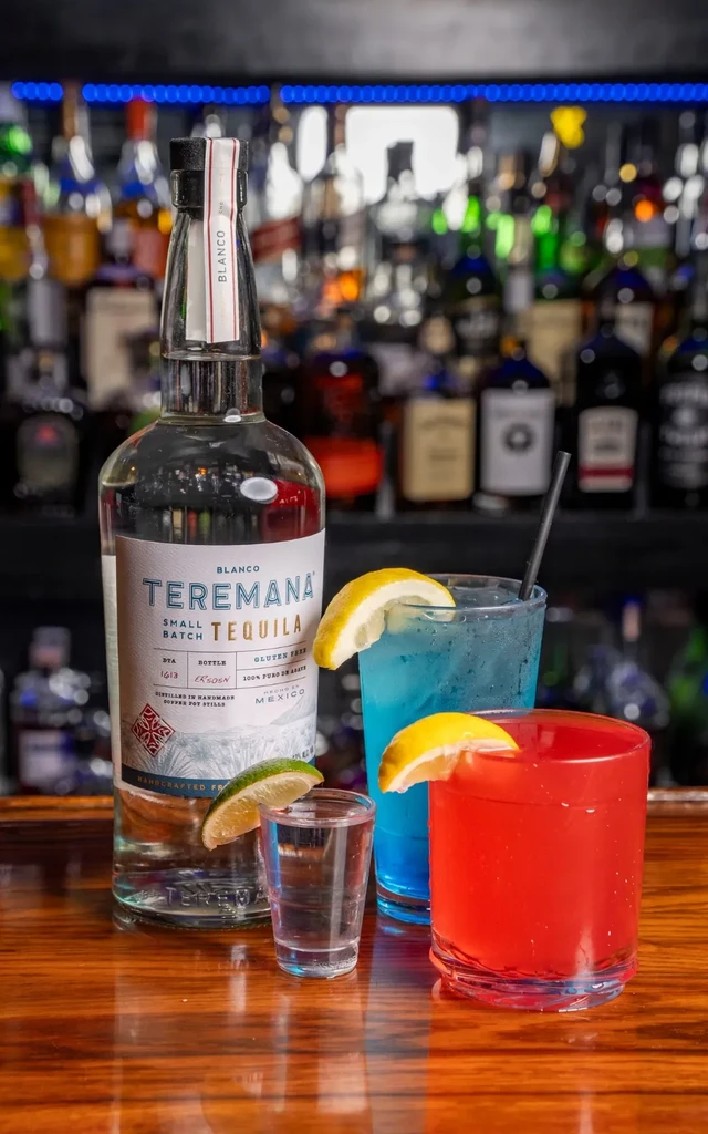 Teremana Blanco tequila bottle, shot, and two cocktails on a wooden bar.