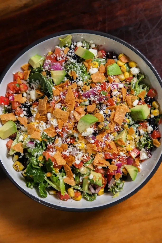 Colorful Southwestern salad with avocado, beans, corn, and tortilla strips.