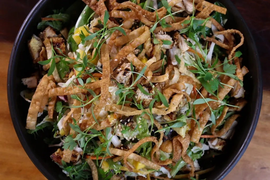 Overhead of vibrant Asian chicken salad with greens, wontons, and sesame.