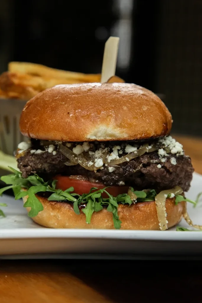 Gourmet burger with blue cheese, caramelized onions, arugula, and fries.