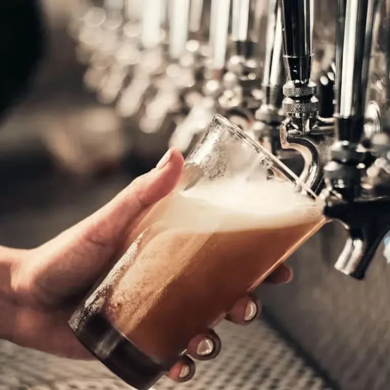 Close-up: hand filling glass with foamy beer from tap.