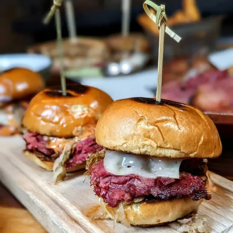 Three gourmet cured meat sliders with skewers on a wooden board.