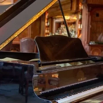 Black Yamaha grand piano, lid open, strings visible, bar background.