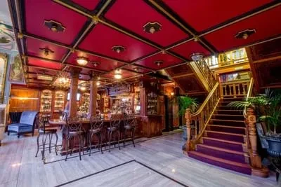 Ornate bar interior with red ceiling, wooden bar, and grand staircase.