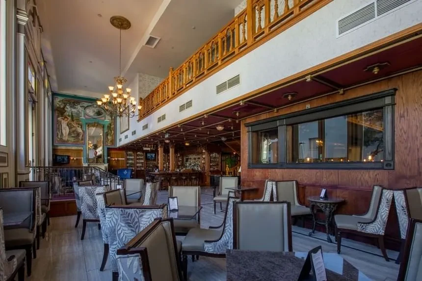 Empty, elegant upscale restaurant interior with bar, mezzanine, chandelier, and mural.