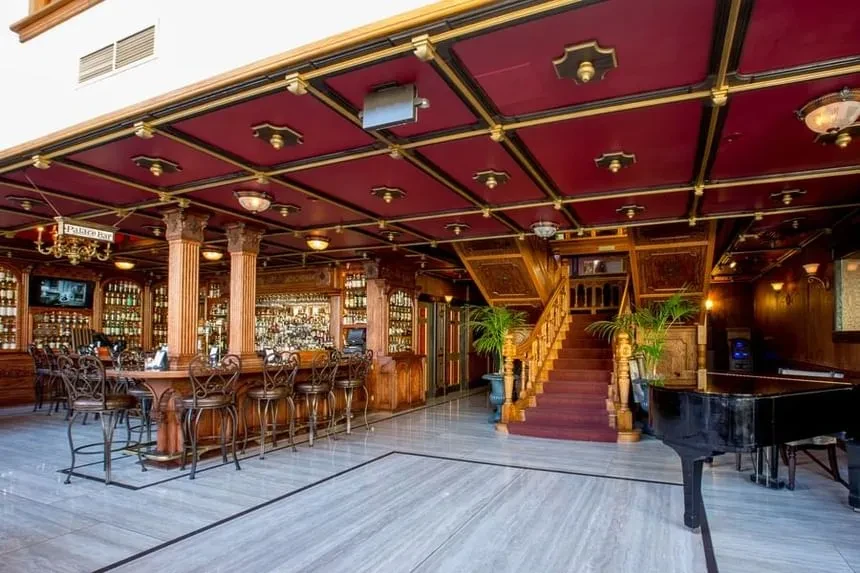 Ornate Palace Bar interior, red ceiling, grand staircase, and piano.