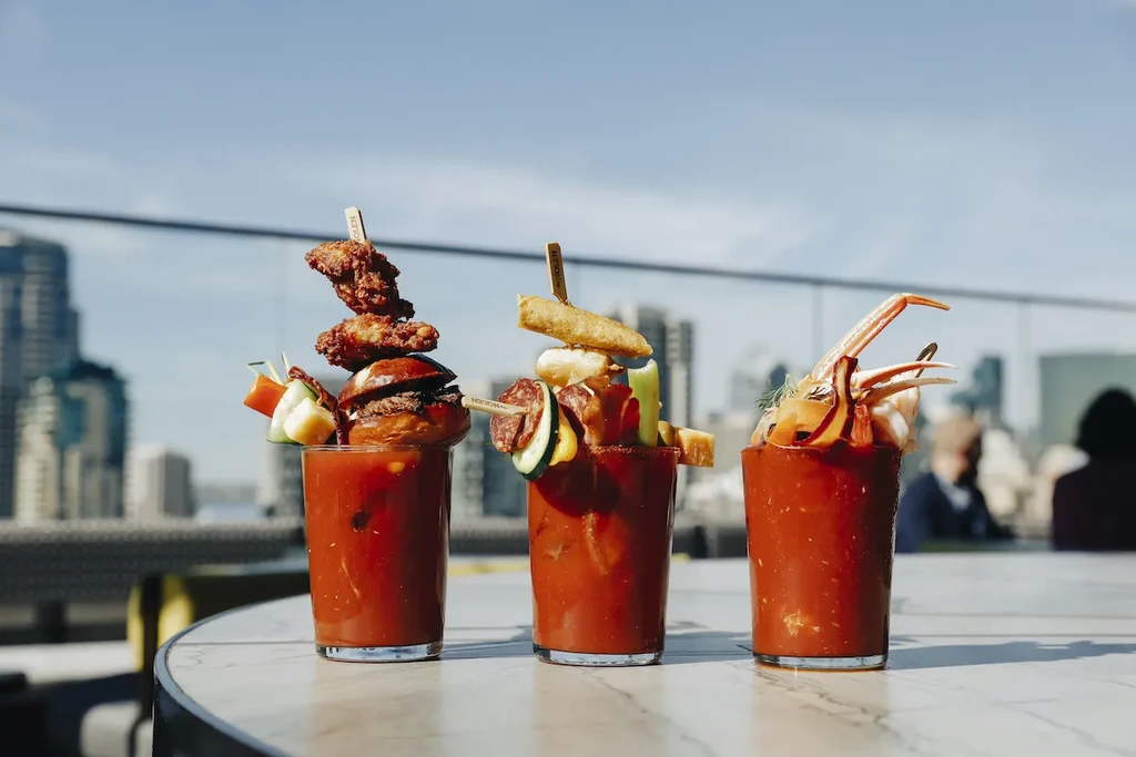 Three elaborately garnished Bloody Mary cocktails on an outdoor patio.