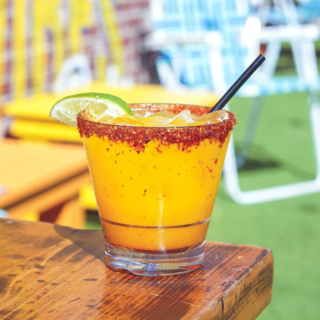 Yellow-orange blended drink with lime, chili rim, ice, and black straw.