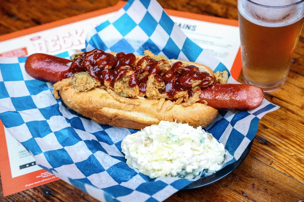 Gourmet hot dog with crispy fried onions, barbecue sauce, potato salad, beer.