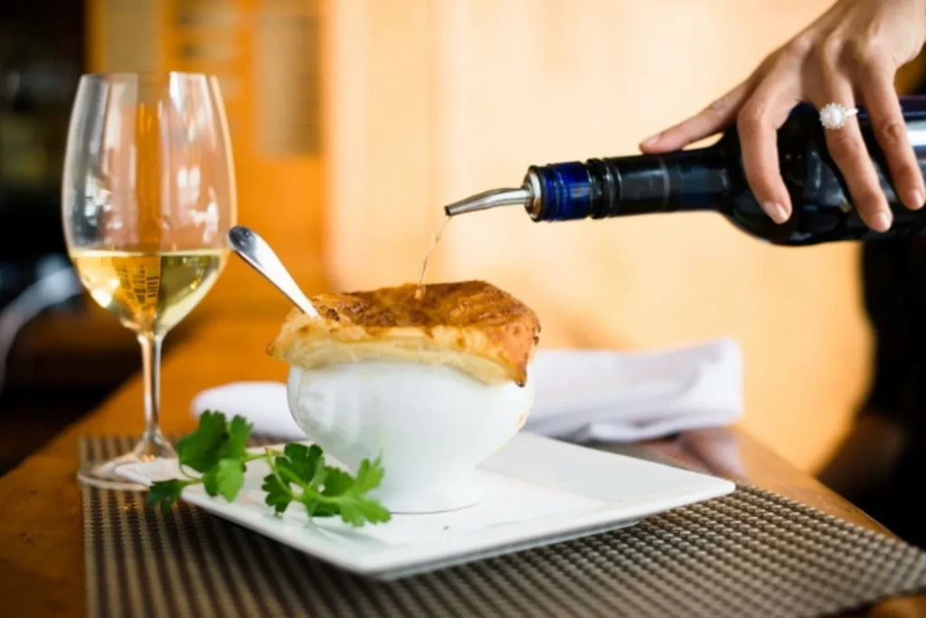 Person drizzles liquid on French onion soup with puff pastry and wine.
