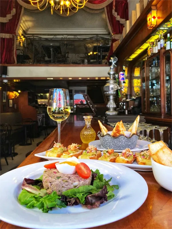 Close-up of tuna tartare and crostini with wine in an ornate restaurant.