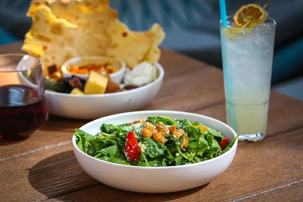 Green salad, drinks, and appetizers on a rustic wooden table.