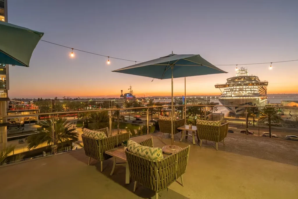 Dusk rooftop patio overlooks a city skyline and brightly lit cruise ship.